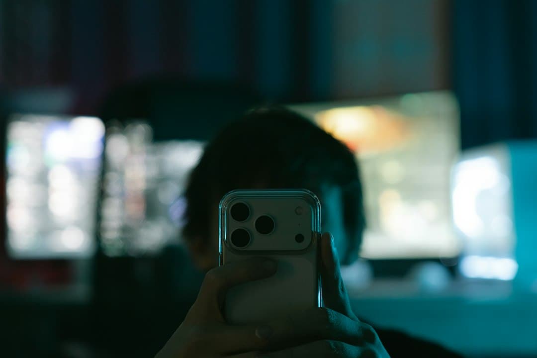 Main tenant un iPhone devant une télévision allumée